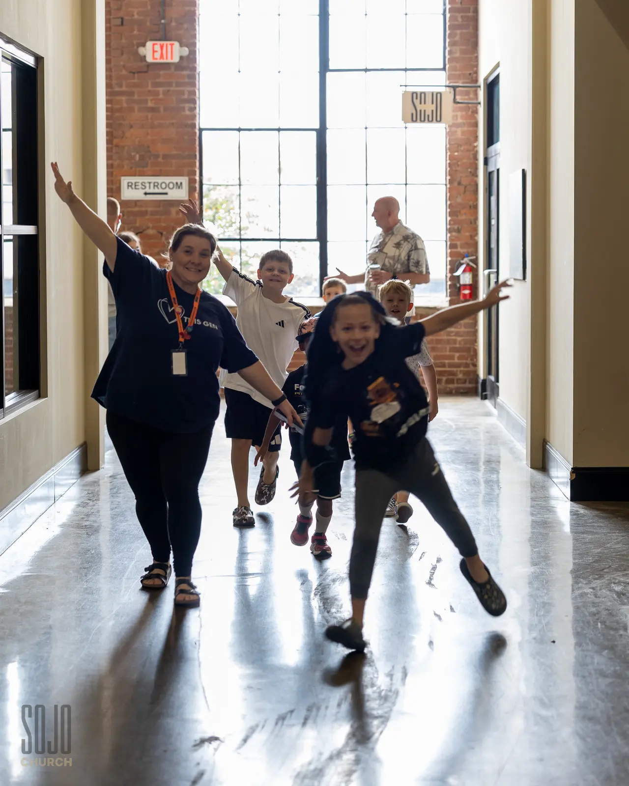 SOJO Kids running down the mill hallway with a leader, arms out like airplanes