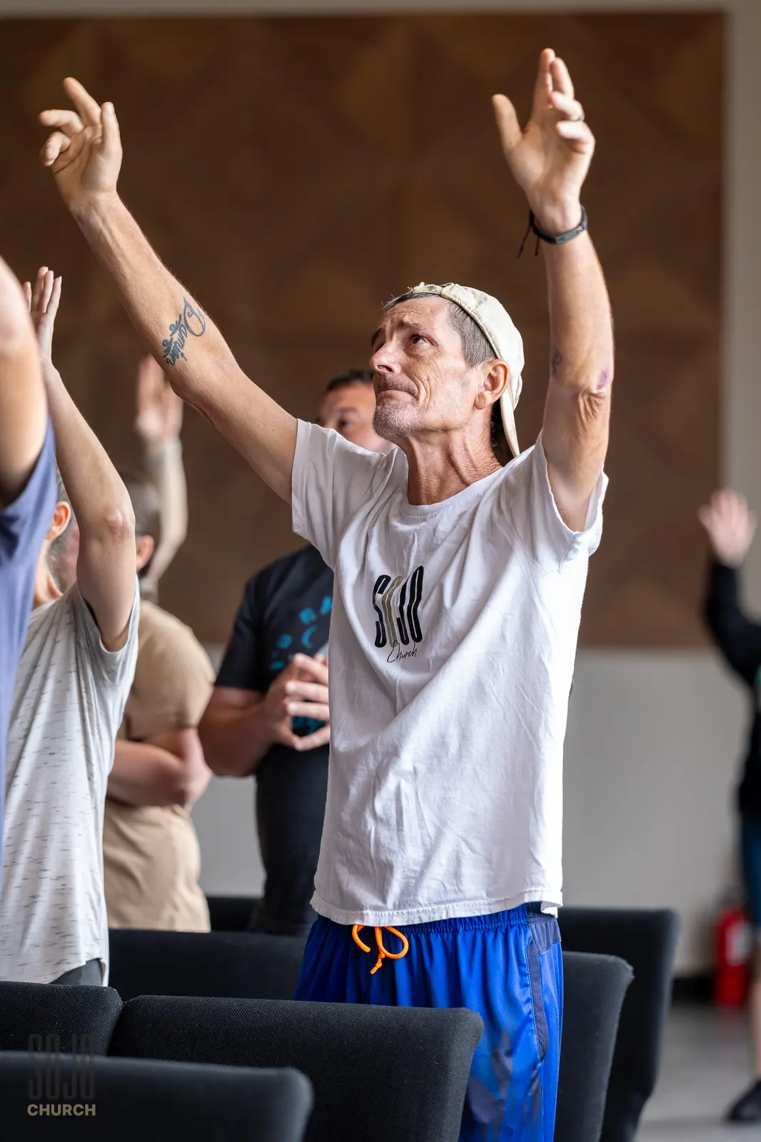 A man in a SOJO shirt with both arms lifted in worship