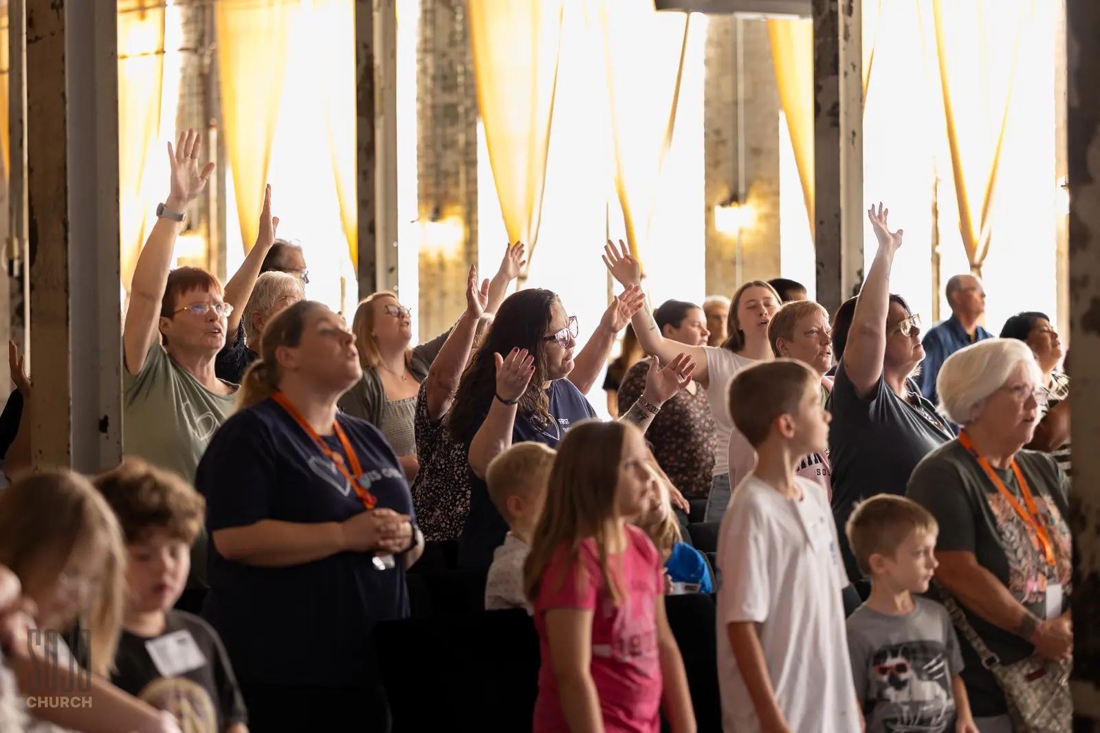 Hands raised in worship at the Kettle Room with gold light through the mill windows
