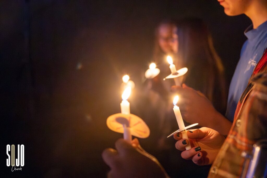 People holding lit candles in a dark room.